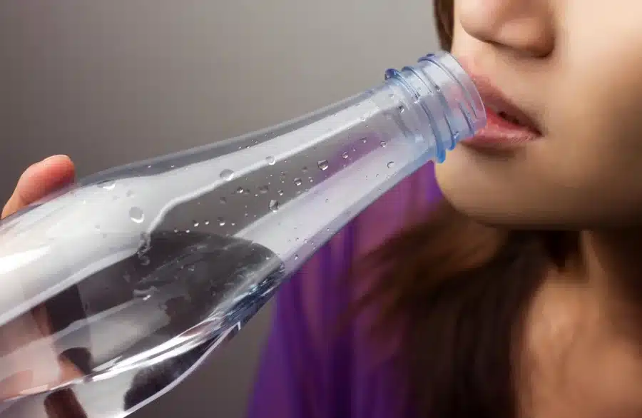 A woman drinking water from a bottle to combat her Dry Mouth a Symptom of Covid