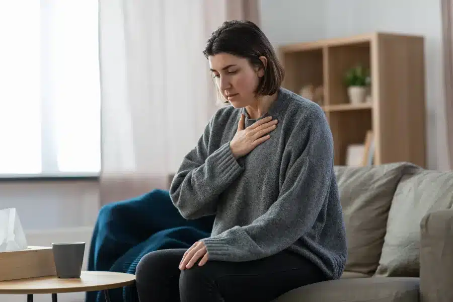 A woman with her hand to her chest appearing to be in discomfort due to Dry Mouth a Symptom of Covid