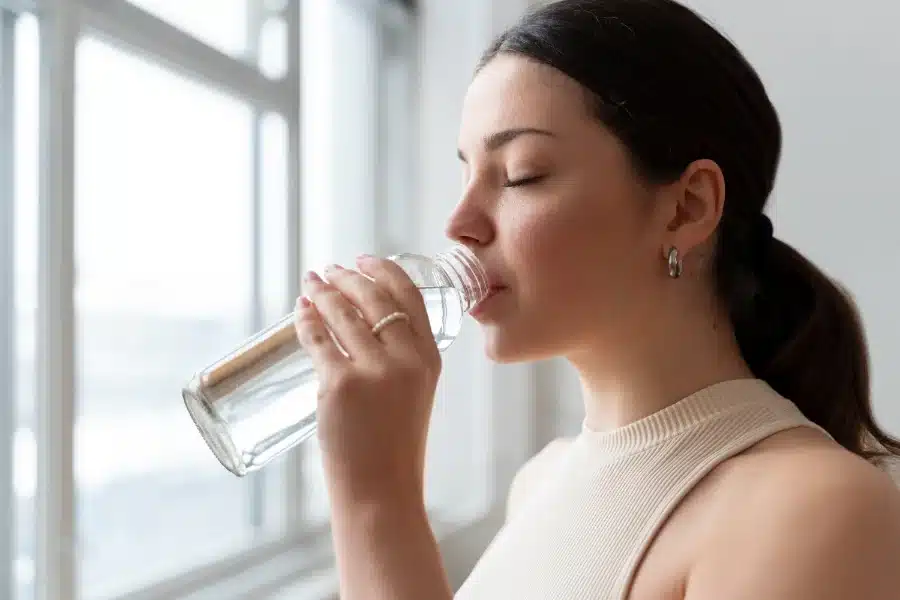 A woman drinking water to temporarily relieve her dry mouth rather than using a product with Hyaluronic Acid which will give her longer lasting relief.