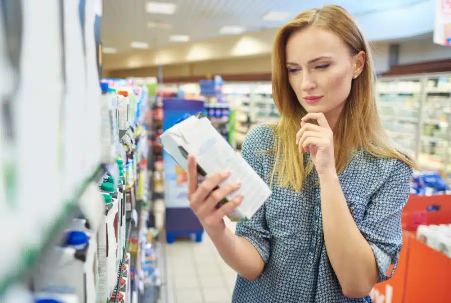 Alt Text: A woman at the grocery store reading the label of a product she picked up off the shelf to make sure it is paraben free.