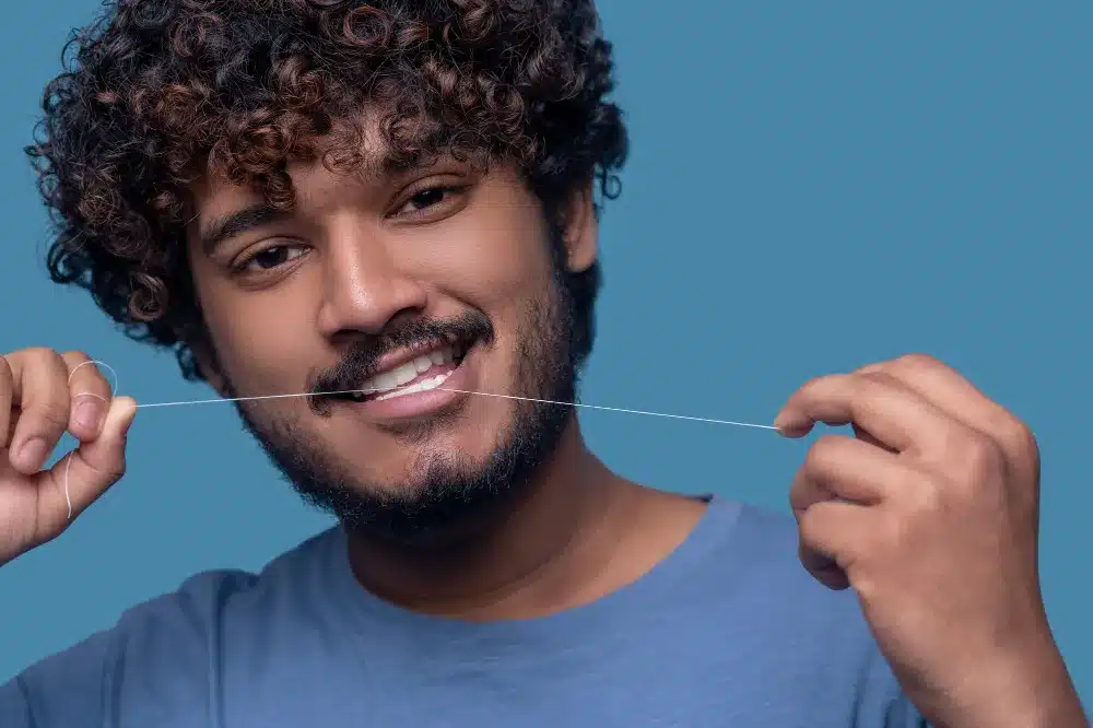 A guy flossing as one method of How To Strengthen Your Teeth.