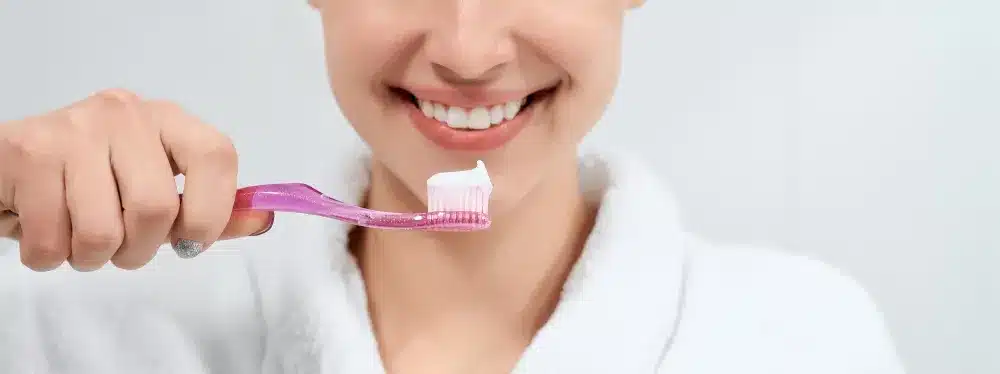 A woman that read this guide on How To Strengthen Your Teeth brushing her teeth with fluoride toothpaste and practicing the other mentioned methods for strengthening tooth enamel. 