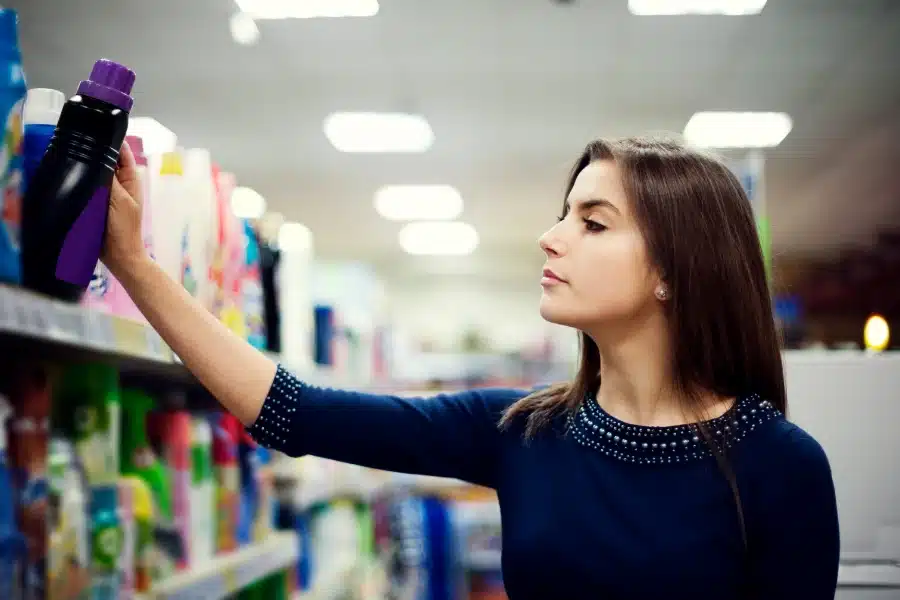 Alt Text: A woman at the supermarket picking up a paraben free and sulfate free laundry detergent.