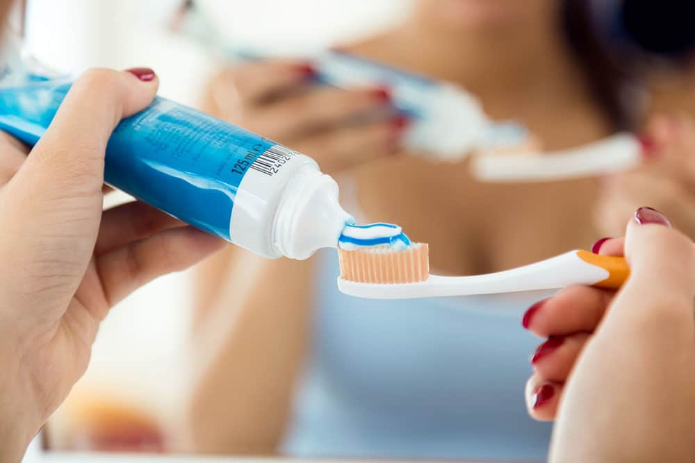 A woman putting toothpaste on a toothbrush before brushing her teeth because she knows about the connection between Oral Health and Breast Cancer. 