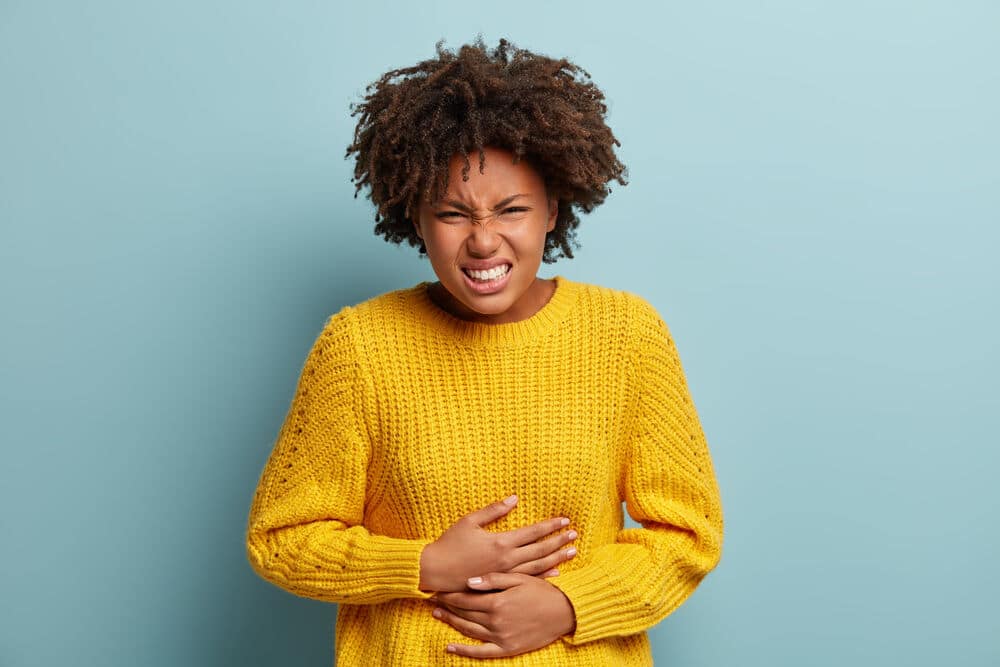 A woman clutching her gut due to stomach pains induced by consuming too much xylitol.