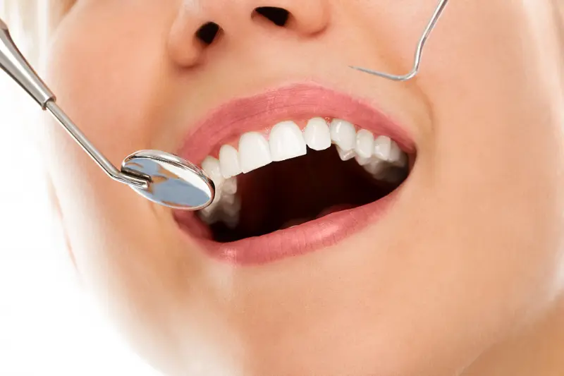 A woman smiling while a dentist examines her smile which appears bright as she’s focused on her oral health